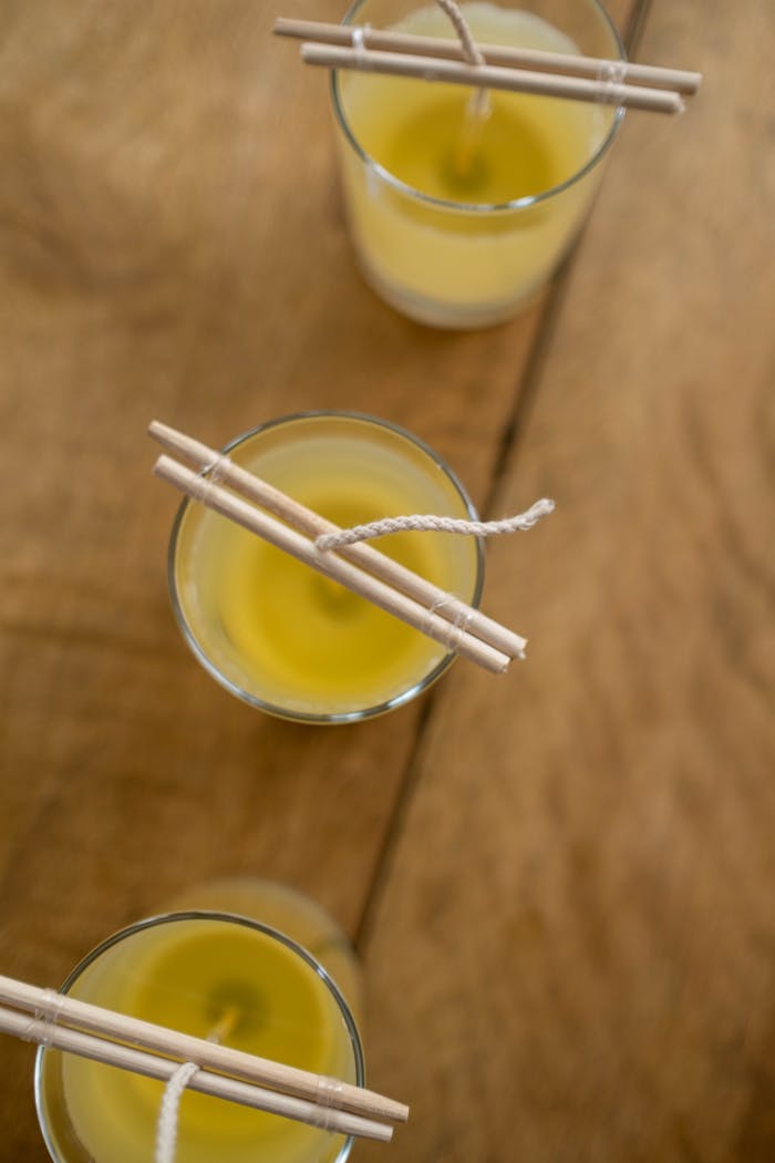 Top view of DIY candle making with yellow wax in clear glass jars on a wooden surface.