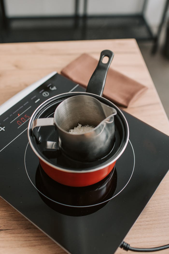 Close-up of a candle wax melting setup on a modern electric stove.